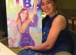 Fotografía real de Alba posando con su regalo de graduación: una ilustración personalizada realizada por Borja Ben para tuvidaencomic.com. Emoción, logro y sonrisa.